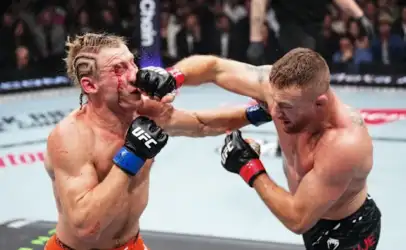 Two UFC fighters clash in the octagon as one lands a punch to the other's face, with visible bleeding from the nose/mouth area.