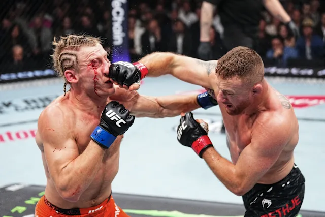 Two UFC fighters clash in the octagon as one lands a punch to the other's face, with visible bleeding from the nose/mouth area.