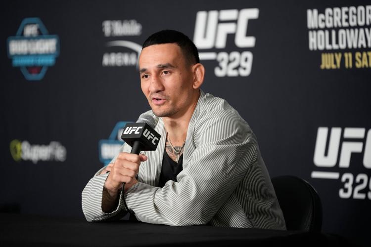 6a50182f820c1image - AfroCombat MMA fighter speaks into a UFC-branded microphone at a press conference, seated at a table with a dark backdrop.