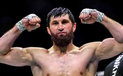 Bearded male mixed martial artist flexing his biceps with fists raised in victory inside the arena.