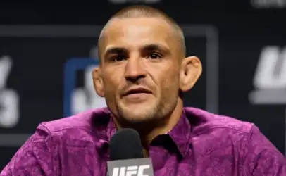 UFC fighter speaks at a press conference, wearing a purple patterned shirt, microphone in front.