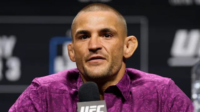 UFC fighter speaks at a press conference, wearing a purple patterned shirt, microphone in front.