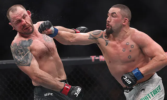 Two UFC fighters clash in the octagon as one lands a punch to his tattooed opponent, gloves on, both shirtless and focused. 2nd fighter grimaces from the hit, cage in the background, arena lighting.