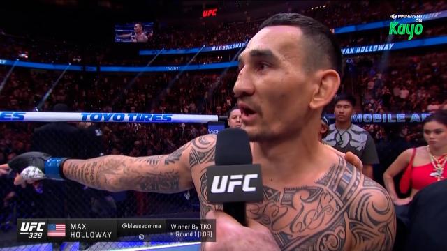 Max Holloway being interviewed in the UFC octagon after a fight, microphone labeled UFC, tattoos on chest visible, arena crowd in the background.