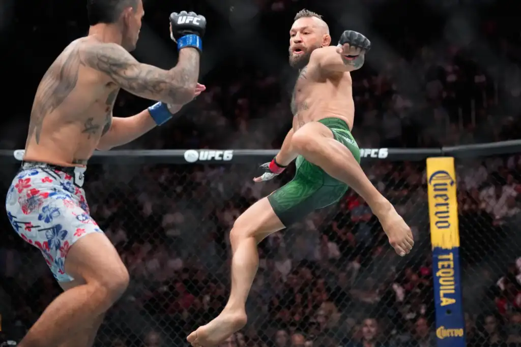 APTOPIX_UFC_329_Mixed_Martial_Arts_53171_ea13f2 - AfroCombat Two MMA fighters in mid-air kicks inside the UFC cage, one in green shorts attacking as the other wearing floral shorts defends with a raised glove.
