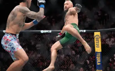 Two MMA fighters in mid-air kicks inside the UFC cage, one in green shorts attacking as the other wearing floral shorts defends with a raised glove.