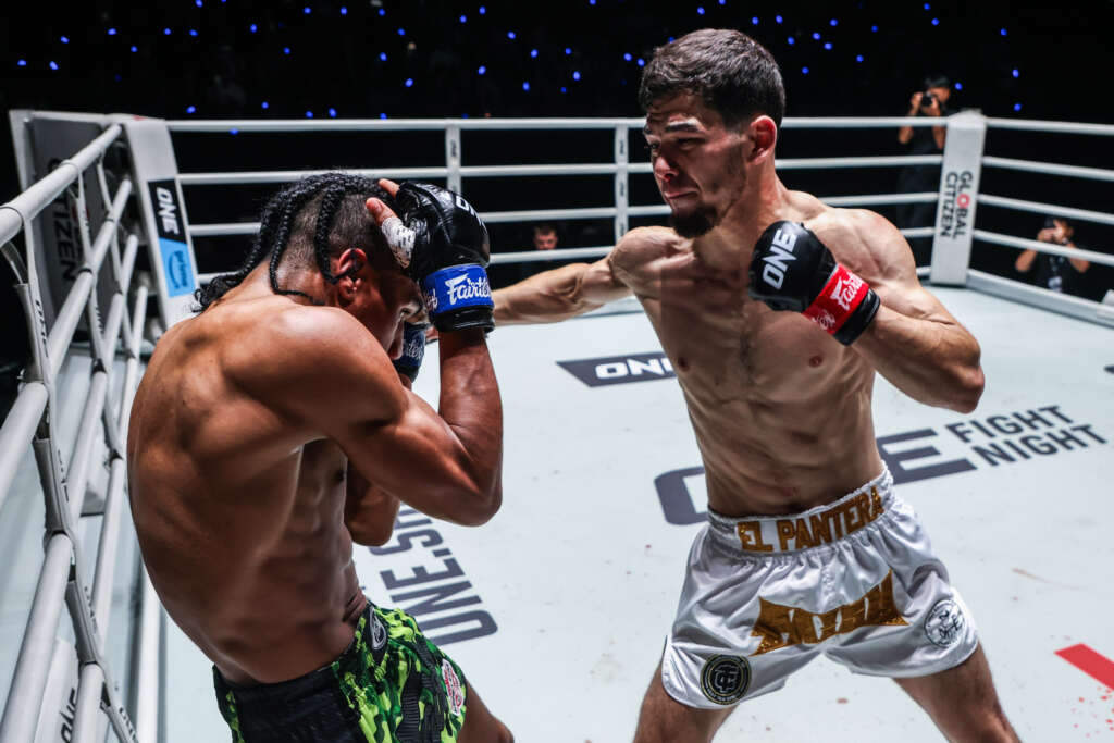 Two shirtless fighters exchange punches inside a boxing ring; one throws a right hand toward the other.