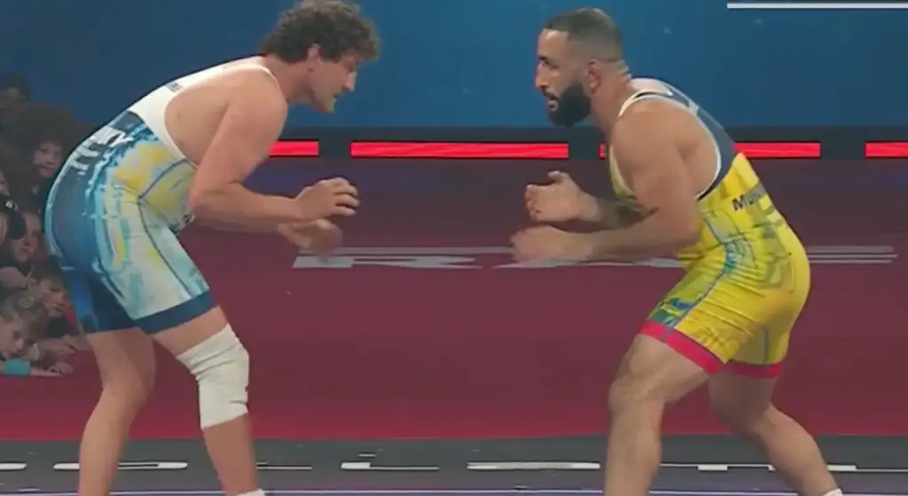 Belal-Muhammad-Ben-Askren - AfroCombat Two muscular wrestlers in a ring face off, crouching and ready to grapple, with spectators in the background.