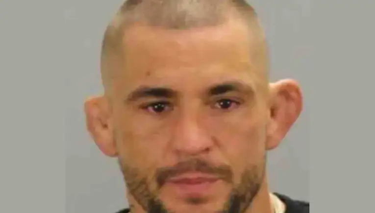 Mugshot of a man with short hair and stubble against a gray backdrop.