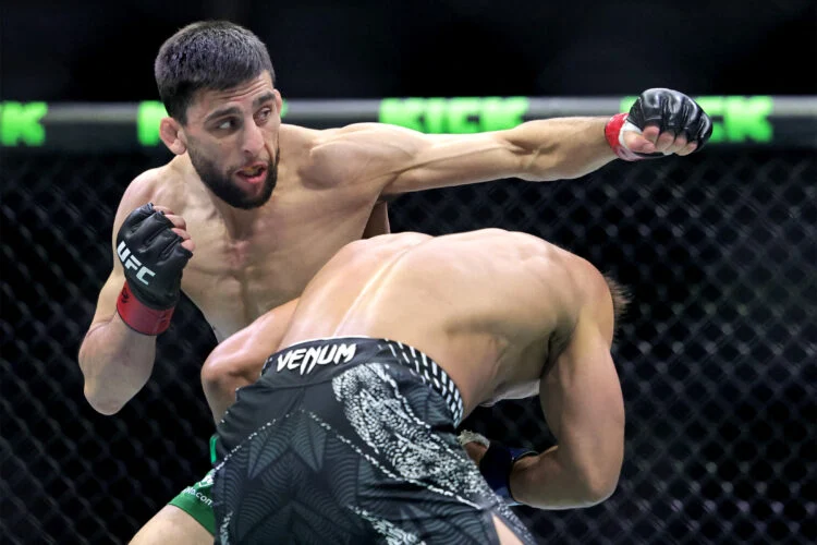 MMA fighters in a cage; one man throws a punch while the other bends forward to avoid it inside the octagon.
