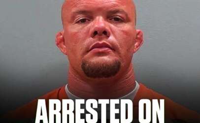 Mugshot of a bald man in an orange jumpsuit against a gray background, with a bold caption reading 'ARRESTED ON 3 FELONY CHARGES' at the bottom and a small circular logo in the top-left corner.