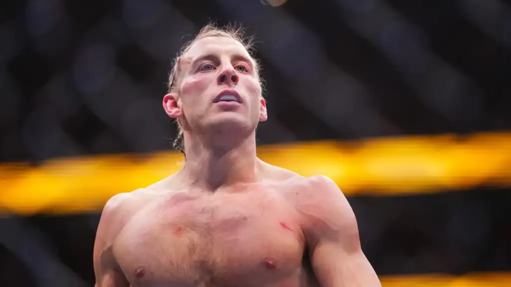 Male mixed martial artist shirtless inside a cage, gazing upward with a determined expression.