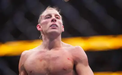 Male mixed martial artist shirtless inside a cage, gazing upward with a determined expression.