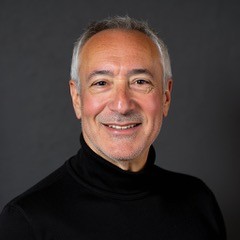 Portrait of a smiling middle-aged man with gray hair in a black turtleneck against a dark background, head-and-shoulders.