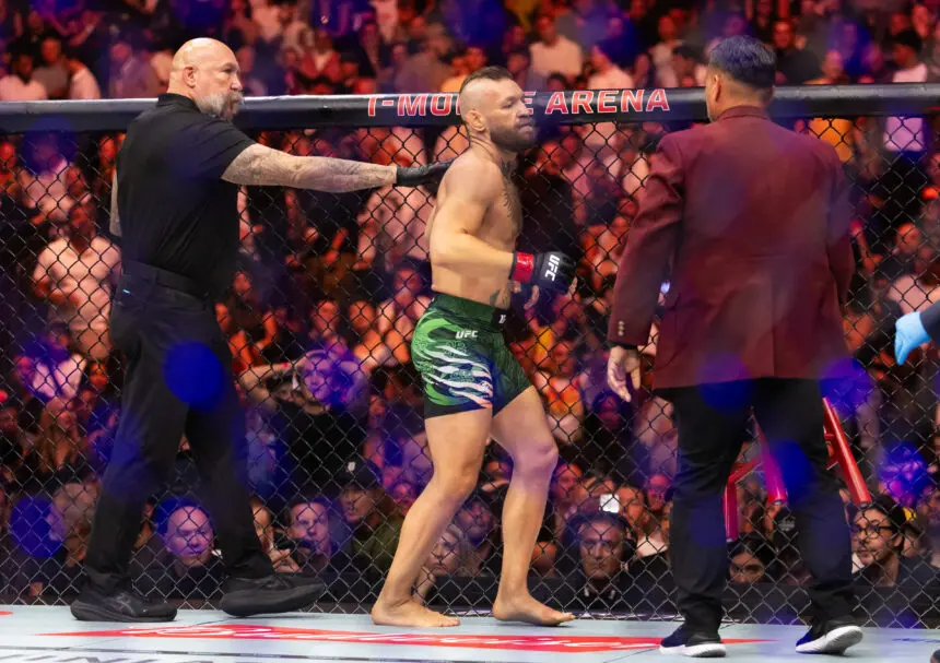 USATSI_29373995-860x607 - AfroCombat UFC fighter in green shorts stands in the cage, flanked by two officials with a cheering crowd behind the mesh fence.