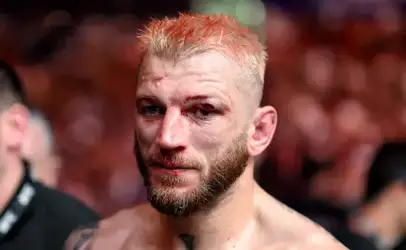 Close-up of a battered male mixed martial artist with short blond hair and a beard, blood on his face in a blurred arena crowd