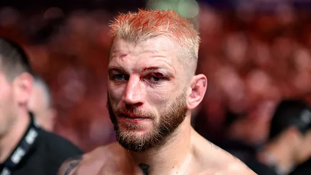 Close-up of a battered male mixed martial artist with short blond hair and a beard, blood on his face in a blurred arena crowd