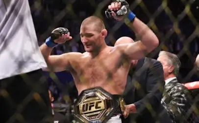 UFC fighter raises fists in victory with championship belt around waist inside an arena