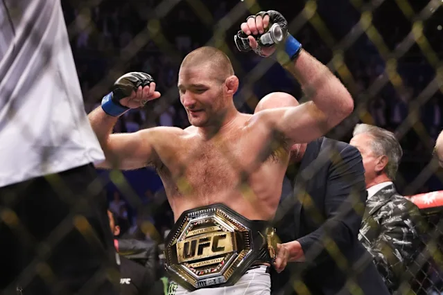 UFC fighter raises fists in victory with championship belt around waist inside an arena