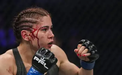 Female MMA fighter with braided hair, glove up, blood streaming down her temple as she stares forward in the cage.