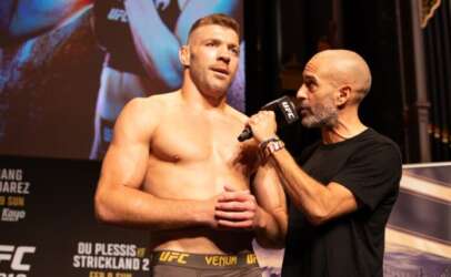 UFC fighter stands shirtless on stage while interviewer holds a microphone to him.