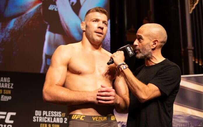 UFC fighter stands shirtless on stage while interviewer holds a microphone to him.