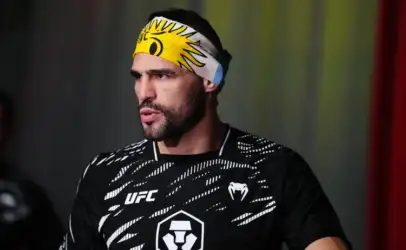 Male UFC fighter wearing a yellow sun-pattern headband and black training jersey with white logos on a dim background