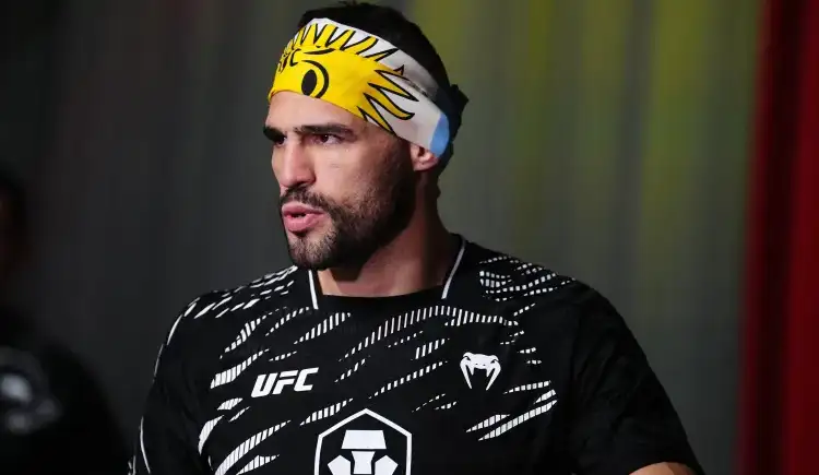 Male UFC fighter wearing a yellow sun-pattern headband and black training jersey with white logos on a dim background