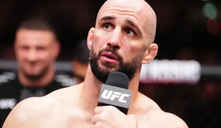 Bald, bearded male MMA fighter speaks into a UFC microphone during a post-fight interview.
