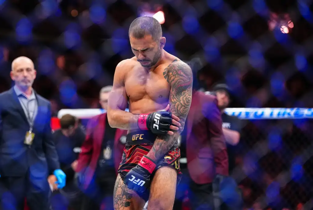 gettyimages-2250450688 - AfroCombat Shirtless UFC fighter with a tattooed left arm stands inside the cage, wearing red and black shorts and UFC gloves, looking down in focus.
