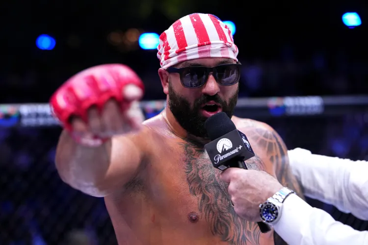 Mixed martial artist in a red-and-white striped bandana and sunglasses gives a post-fight interview inside the cage, microphone near his mouth.