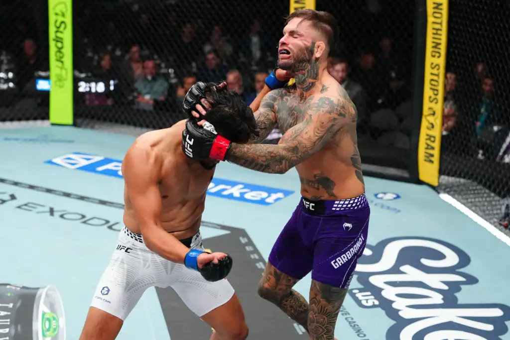 Tattooed UFC fighter in purple shorts applies a headlock on an opponent in white shorts inside the cage.