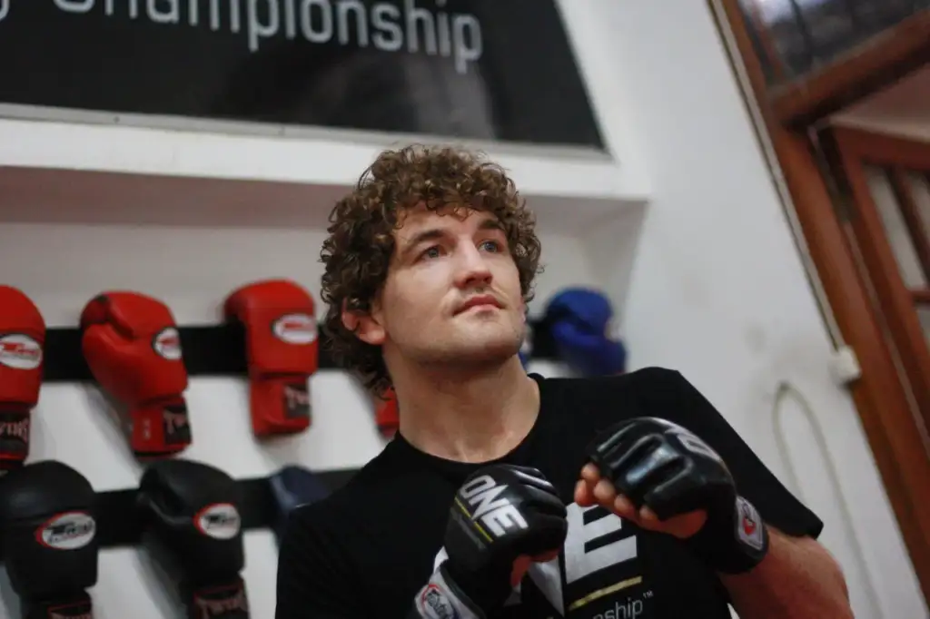 imago16440072 - AfroCombat Young man with curly hair wearing boxing gloves in a gym, standing with fists up near a wall of red gloves and a banner reading Championship (partial).