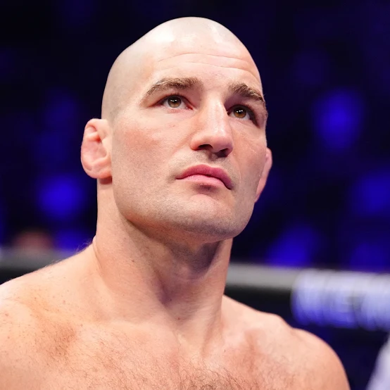 Close-up portrait of a bald male athlete in a boxing ring, looking upward with a focused expression.