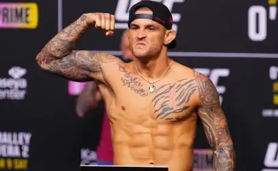 Tattooed male fighter flexing his bicep on a weigh-in stage at a UFC event.