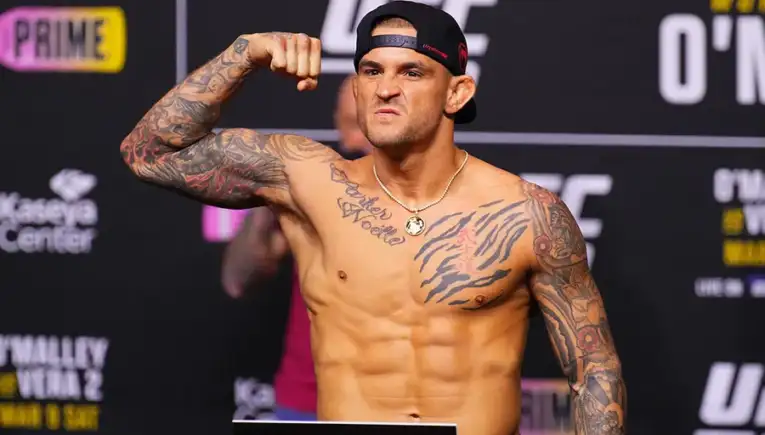 Tattooed male fighter flexing his bicep on a weigh-in stage at a UFC event.
