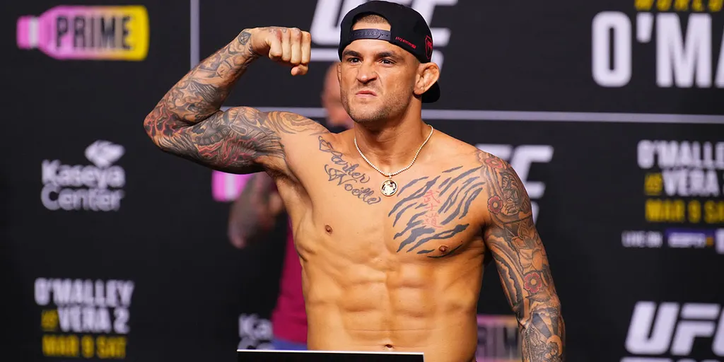 Tattooed male fighter flexing his bicep on a weigh-in stage at a UFC event.