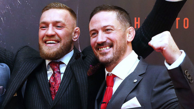 Two men in dark suits and red ties smiling with arms raised in celebration.