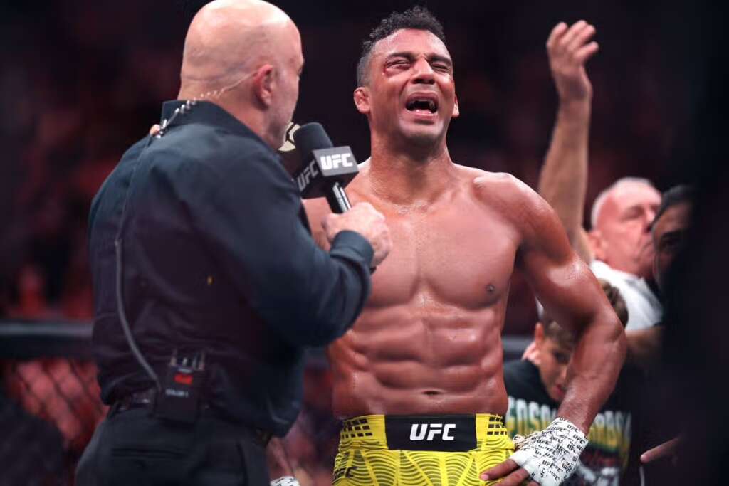UFC fighter with yellow shorts speaks into a microphone held by an interviewer in the octagon after a fight.