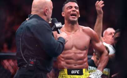 UFC fighter with yellow shorts speaks into a microphone held by an interviewer in the octagon after a fight.