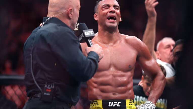 UFC fighter with yellow shorts speaks into a microphone held by an interviewer in the octagon after a fight.