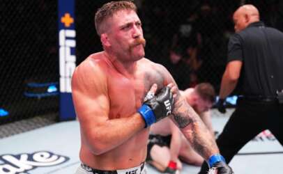 Muscular UFC fighter with blue gloves and tattoos crosses his arms over his chest inside the octagon during a bout.