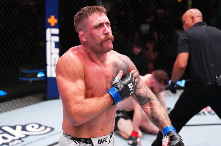 Muscular UFC fighter with blue gloves and tattoos crosses his arms over his chest inside the octagon during a bout.