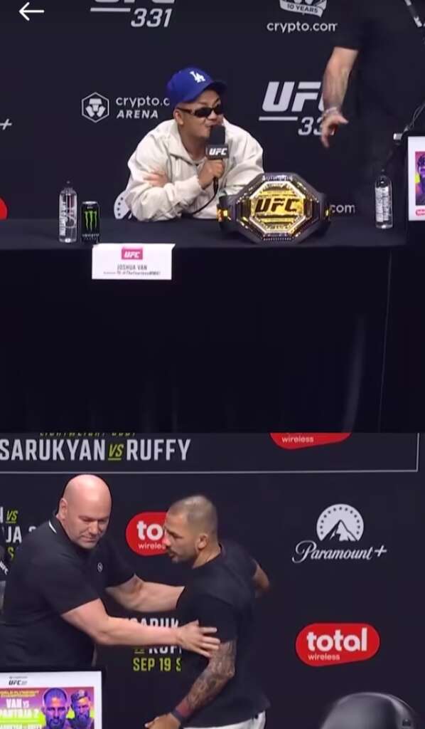 Press conference scene: a man in a blue cap speaks into a microphone with a UFC belt on the table beside him in front of a UFC backdrop.