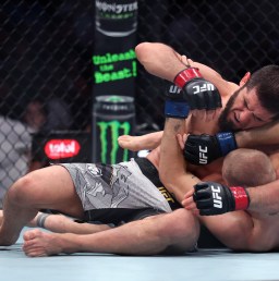 Two UFC fighters grapple on the mat inside the octagon; one on top pins the other in a ground-control position.