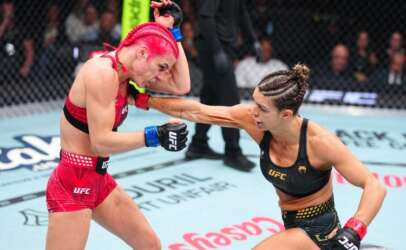 Two female UFC fighters compete inside the octagon as one lands a punch on the other, the red-haired fighter grimacing from impact.