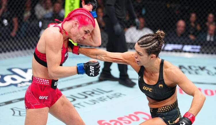 Two female UFC fighters compete inside the octagon as one lands a punch on the other, the red-haired fighter grimacing from impact.