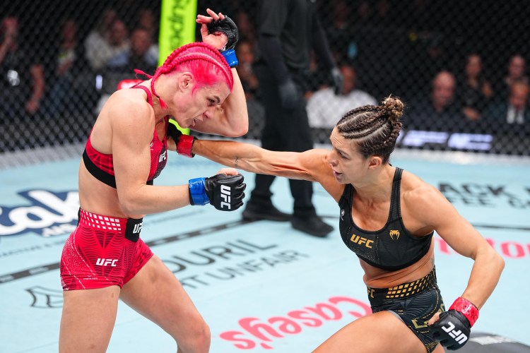 Two female UFC fighters compete inside the octagon as one lands a punch on the other, the red-haired fighter grimacing from impact.