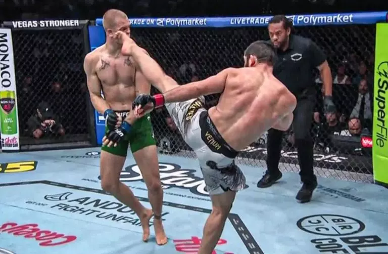 Two shirtless MMA fighters in a cage; one delivers a high kick to the other, who guards his head, as a referee watches nearby.