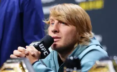 Blond-haired man speaking into a UFC microphone at a press conference with a focused expression.